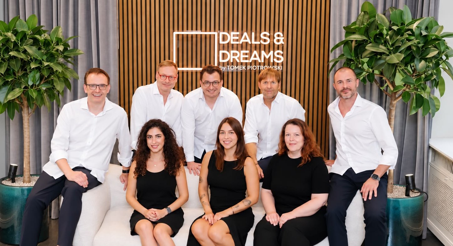 Das Team der Magnolia Group im Büro vor der Deals-&-Dreams-Leuchtschrift
